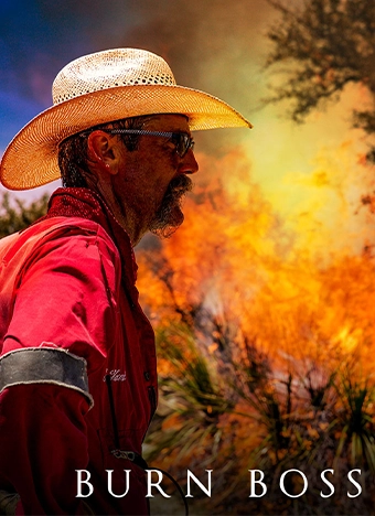 Burn Boss text in white across the bottom of the picture with a man standing in front of a fire that has plants ablaze